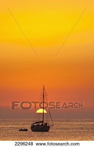 Stock Photo - Spain, People watching sunset from yacht moored off Benirras beach; Ibiza. Fotosearch