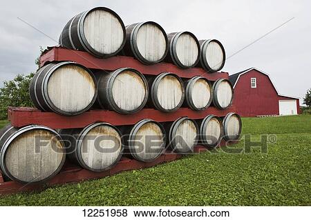 Stacks Of Wooden Barrels With A Red Barn In The Background