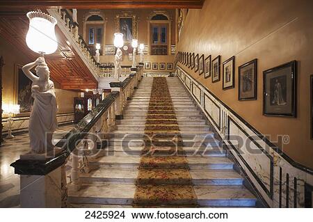 Picture - Staircase with photographs lining the wall and statues on the railing in Falaknuma Palace; Hyderabad, Andhra Pradesh, India. Fotosearch