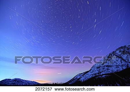 Stock Photo - Star Trails Above A Mountain With Northern Lights On Horizon, Yukon. Fotosearch