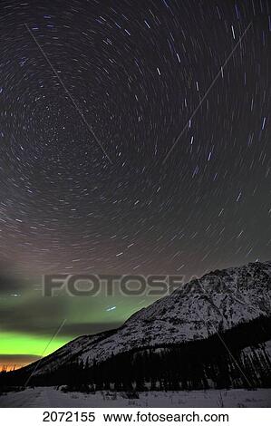 Stock Photography - Star Trails Above A Mountain With Aurora Borealis Or Northern Lights On Horizon, Yukon. Fotosearch