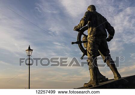 Stock Photo - Statue of sailor turning boat steering wheel at dusk; South Shields, Tyne and Wear, England. Fotosearch