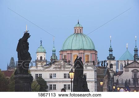 Stock Image - Statues On Charles Bridge With A Church In The Background; Prague, Czech Republic. Fotosearch