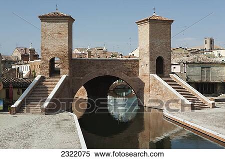 Stock Photography - Stone bridge with towers and steps reflecting in water; Comacchio, Emilia-Romagna, Italy. Fotosearch