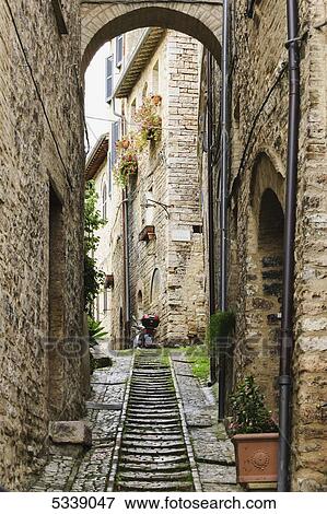 Stock Photo - Stone buildings and cobblestone walkway under an arch; Spello, Umbria, Italy. Fotosearch