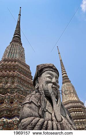 Stock Photo - Stone guard statue and temple spires (chedi) at Wat Pho, the Temple of the Reclining Buddha, the largest Buddhist temple in Bangkok; Bangkok, Thailand. Fotosearch