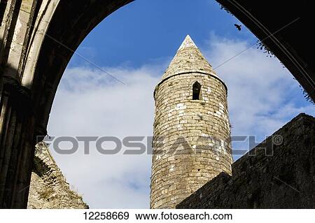 Stock Photo - Stone round tower framed by archway of roofless church with blue sky and clouds; Cashel, County Tipperary, Ireland. Fotosearch