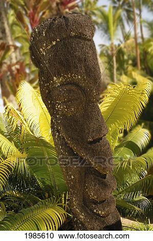 Stock Image - Stone statue nestled among bright palm fronds; Fiji. Fotosearch