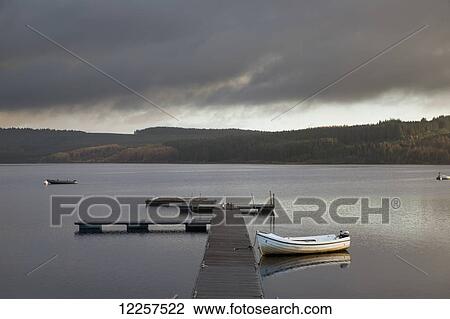 Storm clouds brew over a tranquil lake with a wooden dock and boat moored; Kielder, Northumberland, England View Large Photo Image Stock Image - Storm clouds brew over a tranquil lake with a wooden dock and boat moored; Kielder, Northumberland, England. Fotosearch