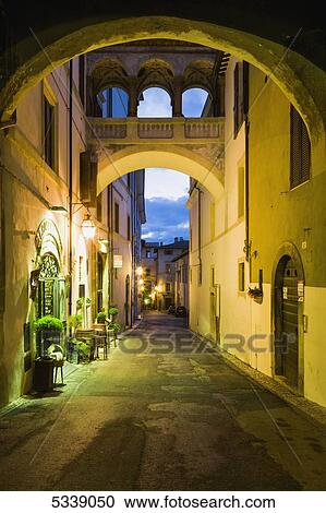 Stock Image - Street between residential buildings illuminated with lights at dusk; Spoleto, Umbria, Italy. Fotosearch