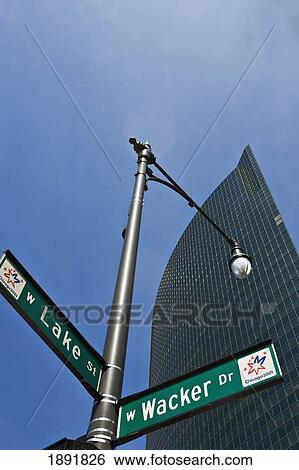Stock Photograph - Street Lamp With Street Signs In Front Of Skyscraper, Low Angle View. Fotosearch