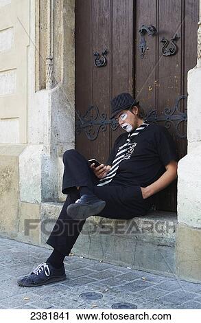Stock Image - Street performer taking a break with cell phone; Krakow, Poland. Fotosearch