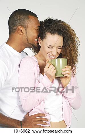 Stock Image - Studio Image Of Couple Whispering With Coffee Cup.. Fotosearch