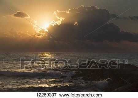 Stock Photo - Sunlight glowing behind clouds at sunrise over the ocean; Paphos, Cyprus. Fotosearch