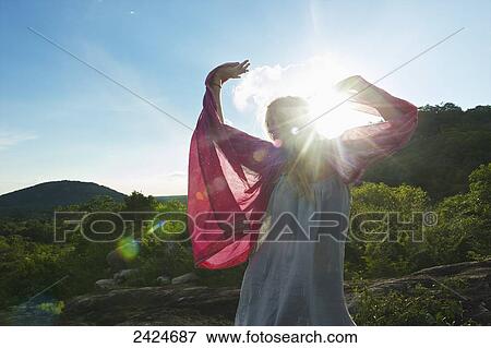 Stock Photo - Sunlight shines over a woman wearing a sheer dress and red shawl; Ulpotha, Embogama, Sri Lanka. Fotosearch