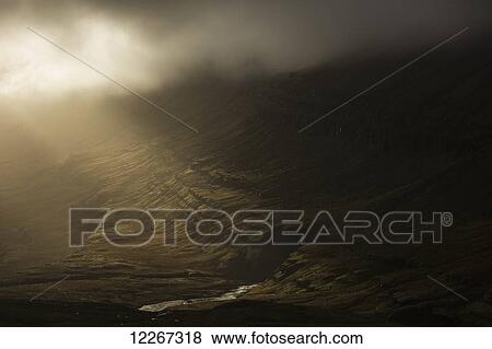 Stock Photo - Sunlight shines through storm clouds and illuminates the hillsides of Iceland's East Fjord region; Iceland. Fotosearch