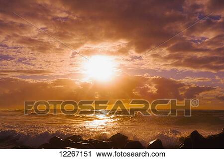 Stock Image - Sunrise and waves crashing on the rocks, Kealia Beach; Kauai, Hawaii, United States of America. Fotosearch