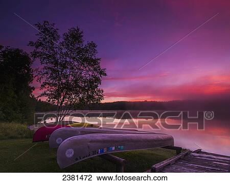 Stock Image - Sunrise explodes over Echo Lake in Aroostook State Park with canoes on the shore; Presque Isle, Maine, United States of America. Fotosearch