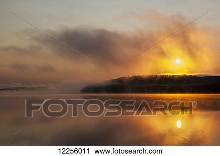 Stock Image - Sunrise over a calm, misty, wilderness lake; Ontario, Canada. Fotosearch