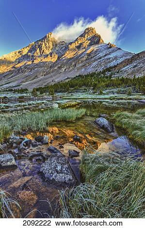 Stock Image - Sunrise Over A Peak Reflected In A Tarn Below Baker Lake In The Skoki Wilderness In Banff National Park; Banff Alberta Canada. Fotosearch