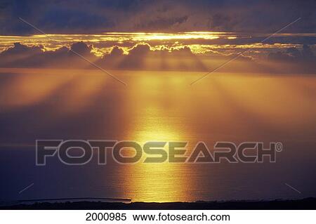 Stock Photography - Sunset Over Calm Ocean Reflections, Rays Beam Out From Behind Clouds. Fotosearch