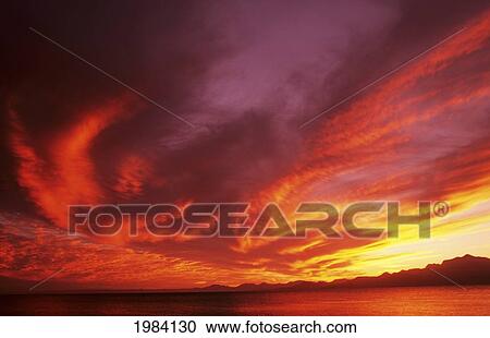 Stock Image - Sunset Over Seascape, Brightly Colored Clouds Illuminated Over Ocean.. Fotosearch
