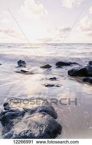 Stock Image - Surf splashing on rocks after sunrise; Wailua, Kauai, Hawaii, United States of America. Fotosearch