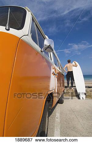 Stock Photo - Surfer And Board Beside Orange And White Old Campervan Parked Beside The Sea. Fotosearch