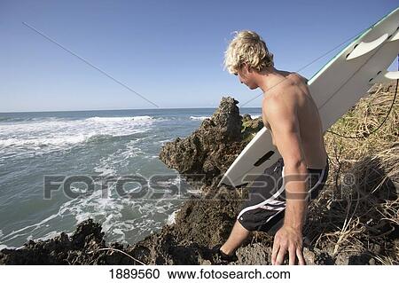 Stock Image - Surfer Crossing Rocks Into The Sea. Fotosearch