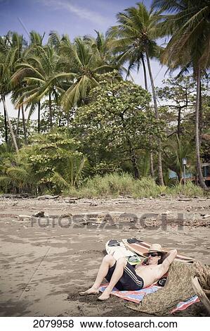 Stock Photo - Surfer Lounges On The Beach; Dominical, Costa Rica. Fotosearch