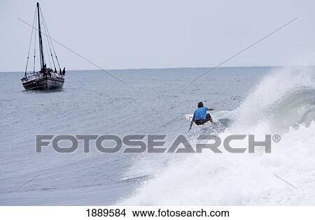 Picture - Surfer Riding Wave With Sailboat Behind. Fotosearch