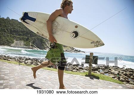 Stock Image - Surfers On The Beach, Victoria Bay, South Africa; Guy Running With Surfboard, Victoria Bay, Garden Route, South Africa. Fotosearch