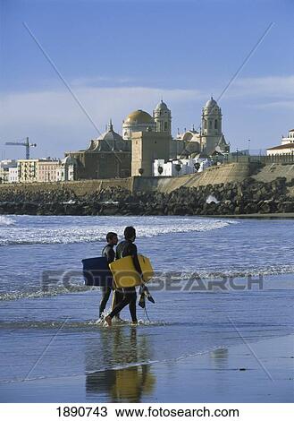 Stock Image - Surfers Walking Ashore In Front Of Santa Cruz Cathedral. Fotosearch