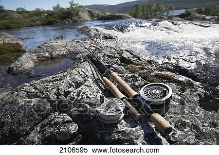 Stock Photography - Sweden, Fishing rods on rock by river; Miekak Lapland. Fotosearch