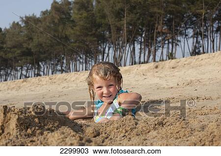 Stock Image - Sylvie Reynolds plays in a hole dug for her to sit in, Turtle Beach, Goa, India.. Fotosearch