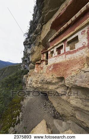 Stock Image - T-shaped windows in a chullpa (stone tomb chamber) of the Chachapoya culture with walls colored with red figures, nestled in the limestone cliffs of Cerro Carb. Fotosearch