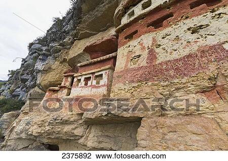 Stock Image - T-shaped windows in the chullpas (stone tomb chambers) of the Chachapoya culture with walls colored with red figures, nestled in the limestone cliffs of Cerro Carb. Fotosearch