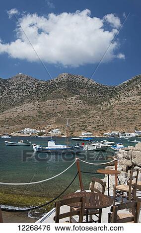 Stock Photograph - Taverna tables and chairs on a stone pier in the port of Kamares; Kamares, Sifnos, Cyclades, Greek Islands, Greece. Fotosearch