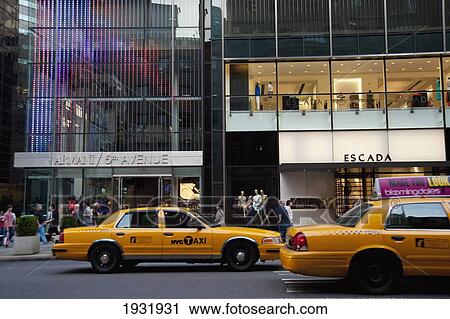 Stock Image - Taxis Passing By Some Designer Shops In 5Th Avenue, Midtown Manhattan, New York, Usa. Fotosearch