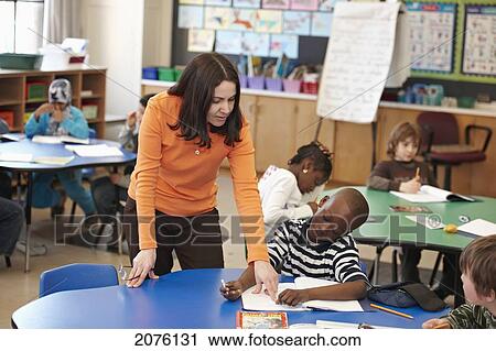Stock Image - Teacher Helping Young Grade 3 Boy At His Desk In Classroom; Toronto Ontario Canada. Fotosearch