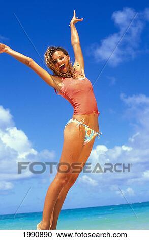 Stock Image - Teen Girl Jumping With Joy Blue Sky And Turquoise Ocean In Background. Fotosearch
