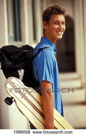 Stock Photo - Teenage Boy Walking With Backpack, Holding Skate- Board. Side Angle View.. Fotosearch