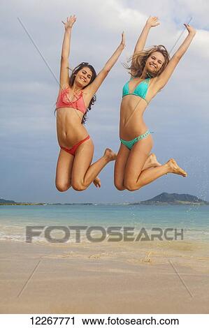 Stock Image - Teenage sisters at the beach jumping in the air; Kailua, Island of Hawaii, Hawaii, United States of America. Fotosearch
