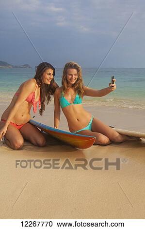 Stock Image - Teenage sisters at the beach with cell phone; Kailua, Island of Hawaii, Hawaii, United States of America. Fotosearch