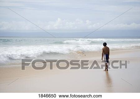 Stock Image - Teenager Looking At Surf On Beach. Fotosearch