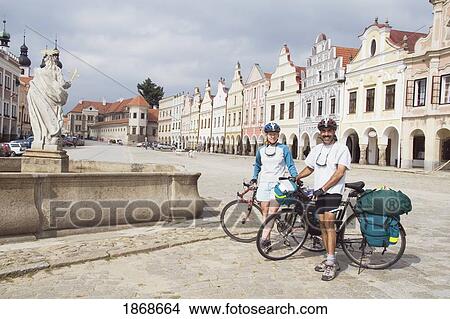 Picture - Telc, Moravia, Czech Republic; A Couple Cycling With Bike Bags In Telc's Town Square. Fotosearch