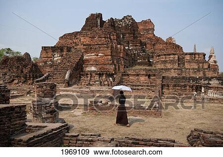 Stock Photo - Thailand, Ayutthaya, Woman visitor with umbrella at Wat Mahathat Buddhist temple ruins.. Fotosearch
