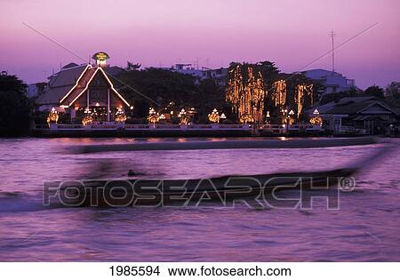Picture - Thailand, Bangkok, Sala Rim Naam Restaurant Lit Up At Evening, Blurred Boat On Chao Phraya River In Foreground.. Fotosearch