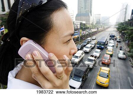 Stock Image - Thailand, Bangkok, Thai Woman Talks On Cell Phone Above Busy Street.. Fotosearch