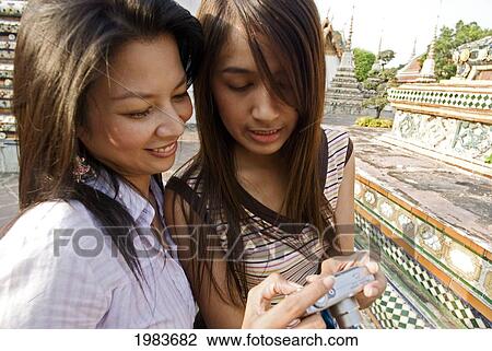 Stock Image - Thailand, Bangkok, Thai Women Looking At The Back Of A Digital Camera.. Fotosearch